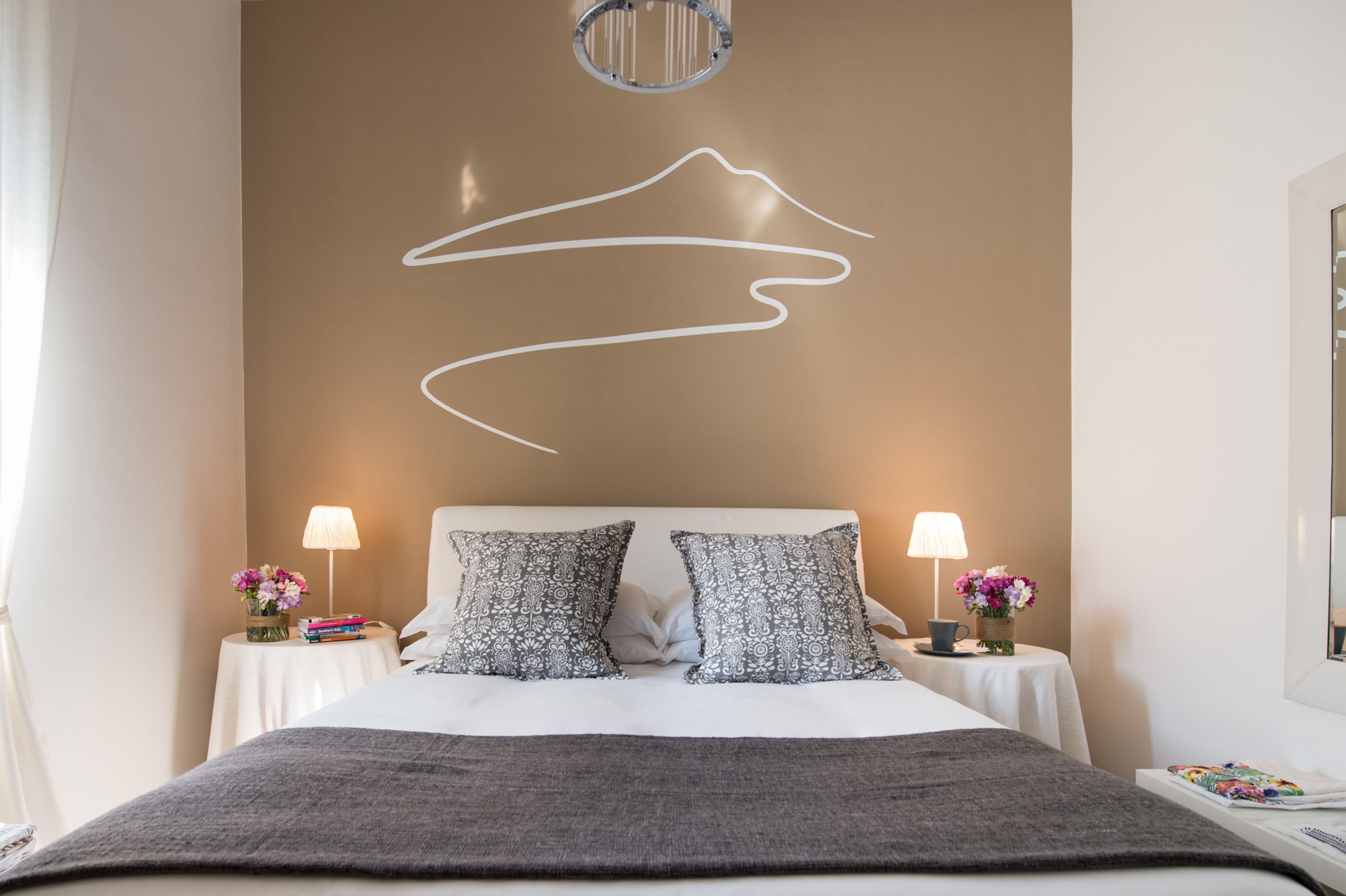 Een moderne hotelkamer met een groot bed, twee nachtkastjes met lampen, gestreepte kussens en een kunstwerk aan de muur.