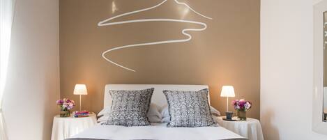 A modern hotel room with a large bed, two bedside tables with lamps, patterned pillows, and a wall art piece.