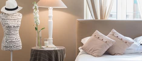 Quarto de hotel com uma cama, uma mesa de cabeceira com abajur, um manequim e uma tigela de maçãs verdes.