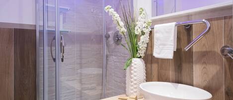 A modern bathroom with a glass shower enclosure, a white sink, and a wooden vanity.