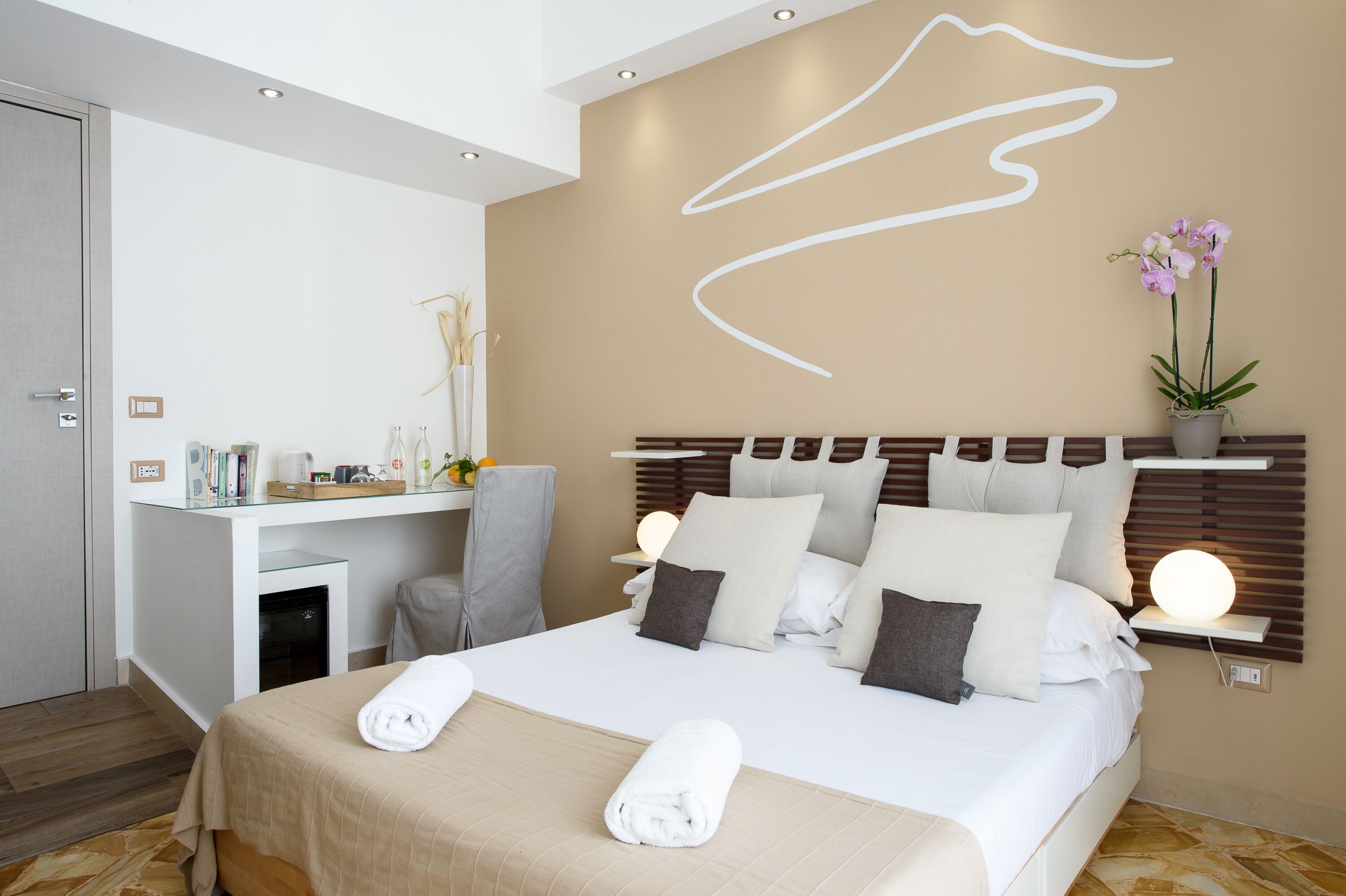 Une chambre d’hôtel moderne avec un lit bien fait, un bureau avec une chaise et une table de chevet avec une lampe.