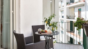 Un balcon avec des fauteuils en osier, une table garnie de fruits et une carafe, ainsi que des plantes en pot.