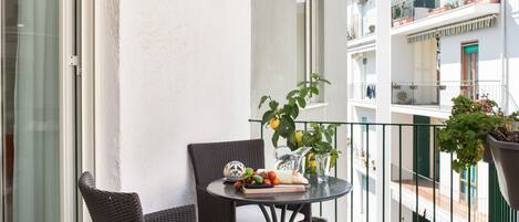 A balcony with wicker chairs, a table with fruits and a pitcher, and potted plants.