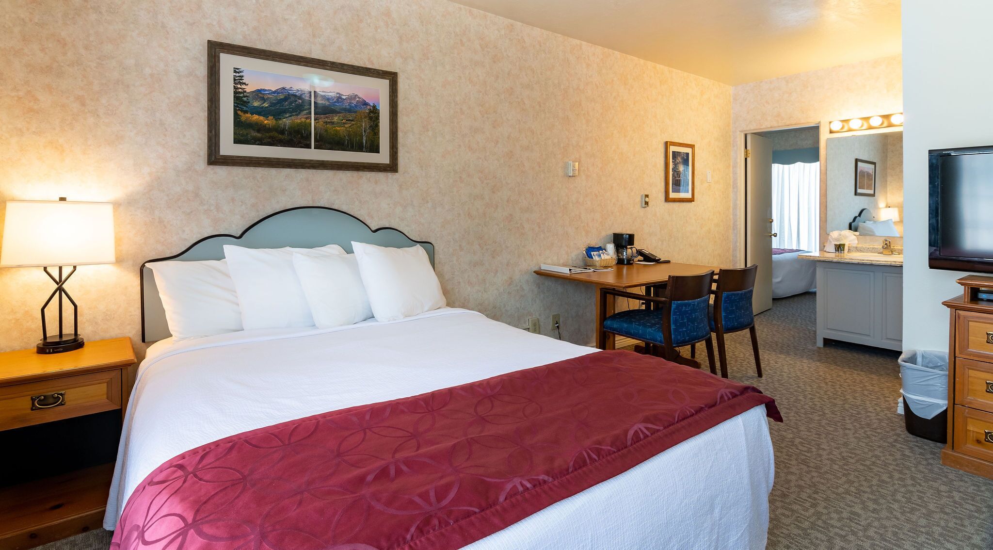Une chambre d’hôtel avec un lit, un bureau, une chaise, une télévision et une salle de bain visible à travers une porte ouverte.
