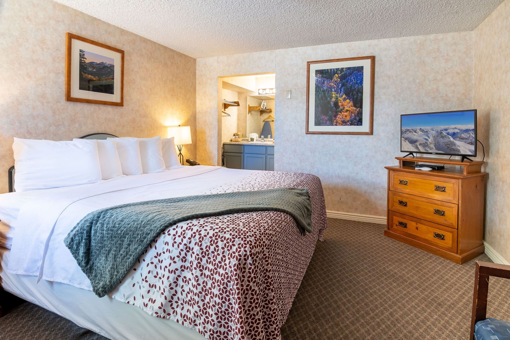 Una habitación de hotel con una cama grande, un aparador, un televisor y dos cuadros en las paredes.