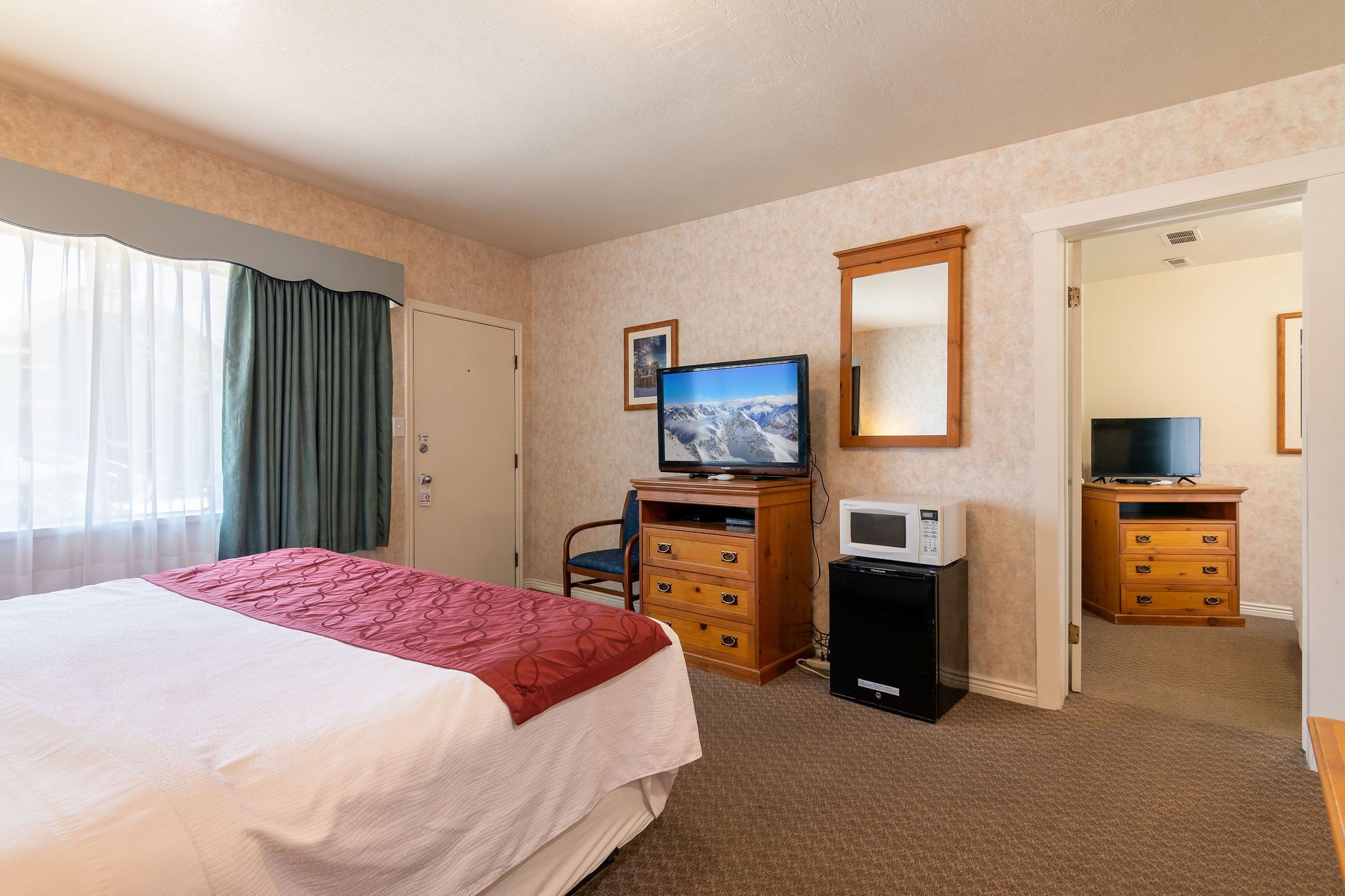 A hotel room with a bed, a desk with a television, a microwave, and a dresser.