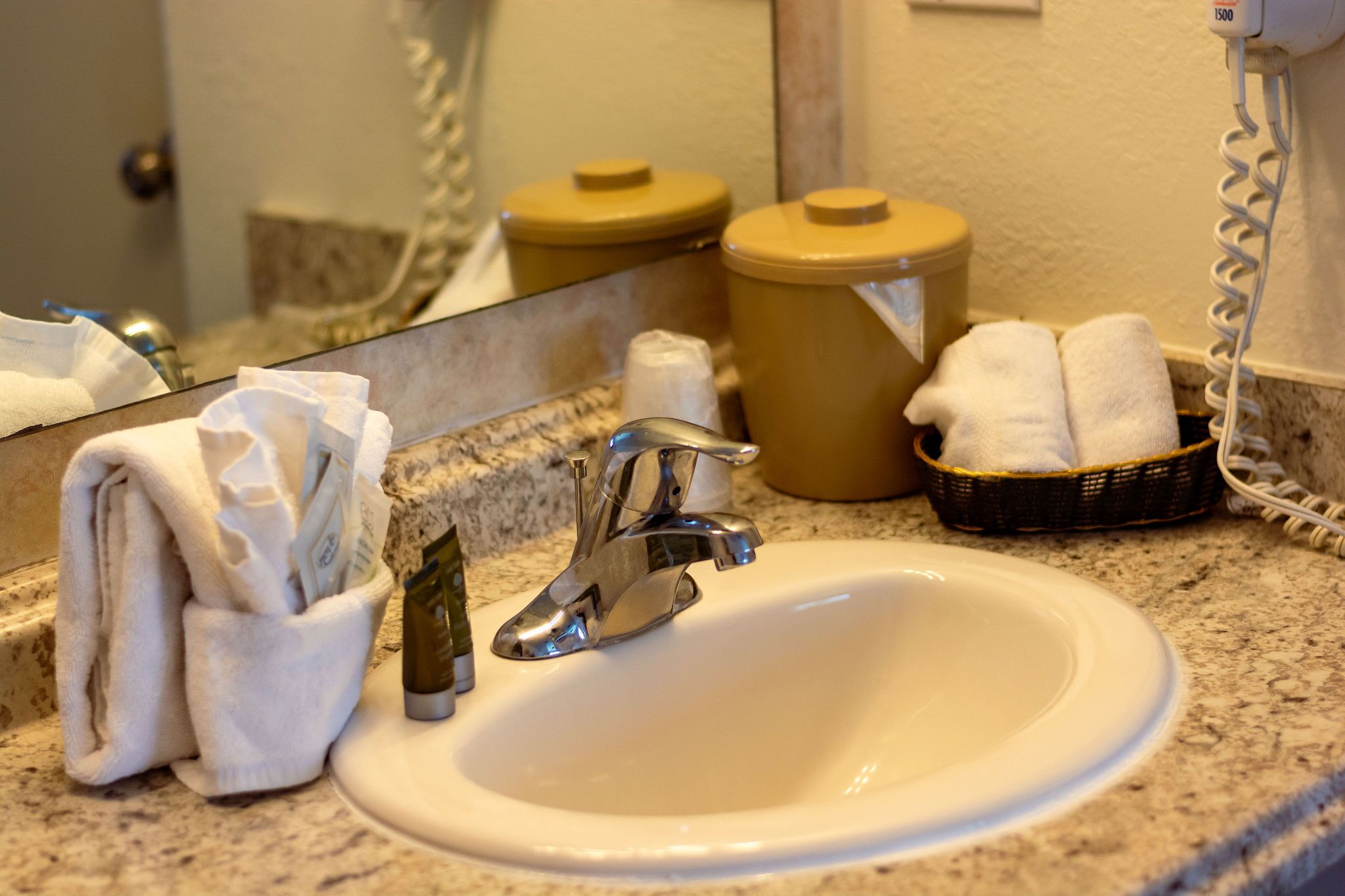 A bathroom sink with a mirror, a towel dispenser, and a basket of towels.
