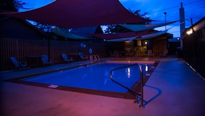 En swimmingpool med ett område som ger skugga, solstolar och ett staket av trä.