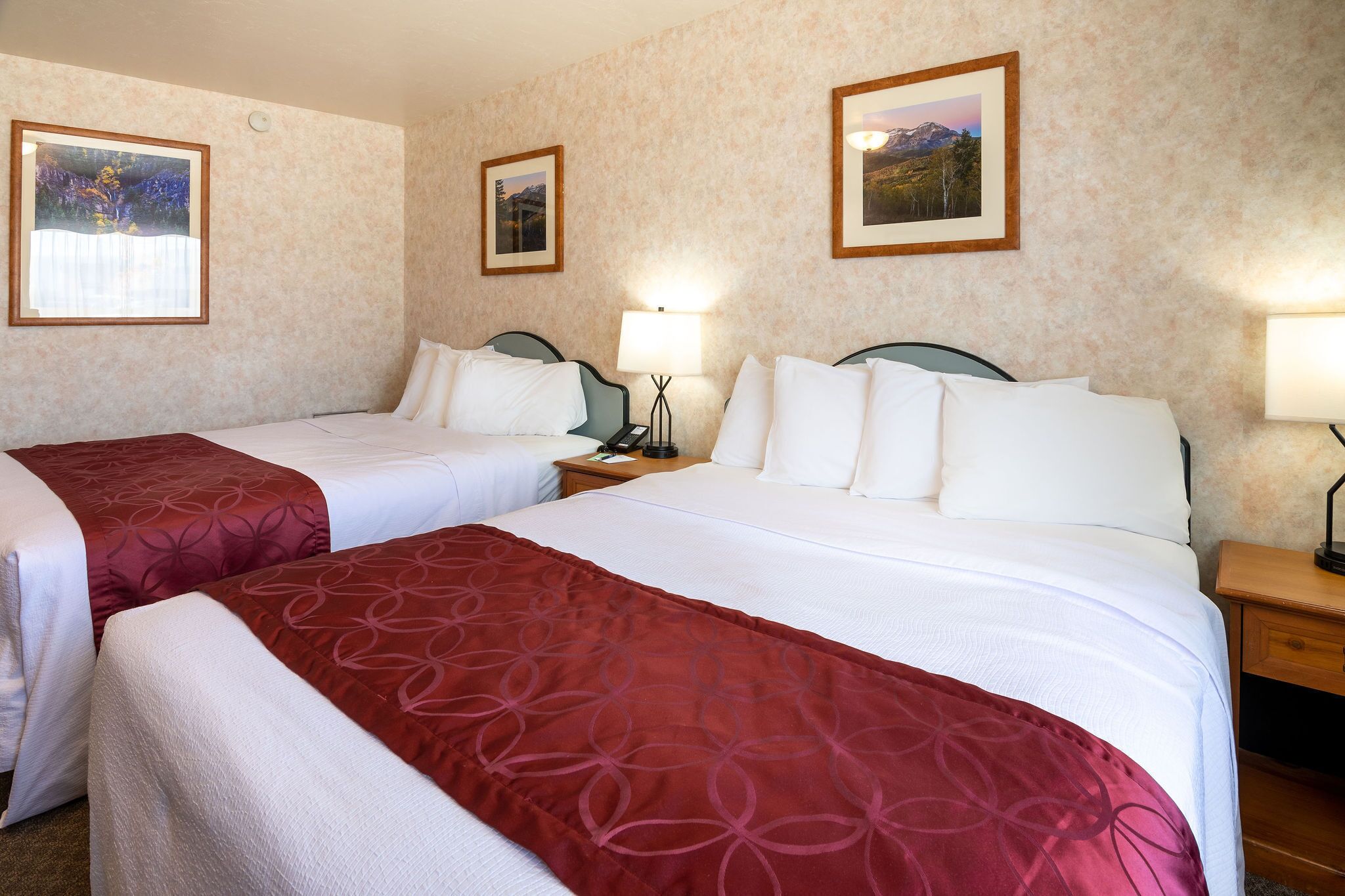 Una habitación de hotel con dos camas, cada una con cubrecama rojo y blanco, y una mesita de noche con lámpara entre ellas.