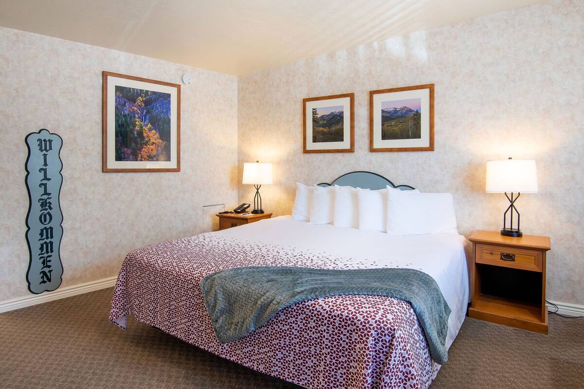 A neatly made bed with a patterned bedspread, two bedside lamps, and framed pictures on the wall.
