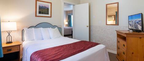 Une chambre d’hôtel avec un lit, un bureau équipé d’un ordinateur, une lampe, un miroir et un tableau encadré au mur.