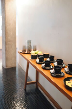 A wooden table with black cups and saucers, a bowl of apples, and a glass container. - CasaSur Palermo Hotel (Buenos Aires)