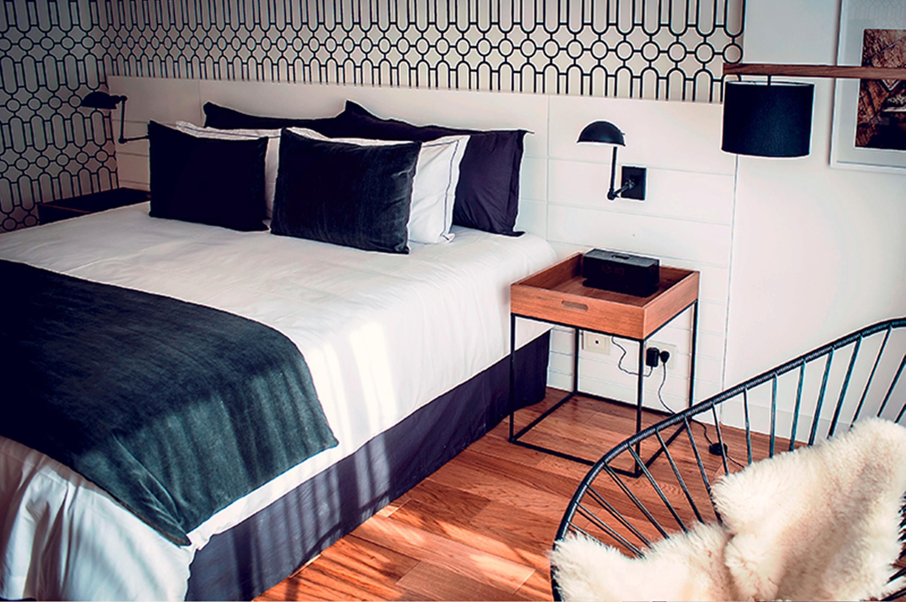 A modern hotel room with a neatly made bed, a bedside table with a lamp, and a chair.