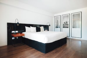 Un dormitorio moderno con una cama grande, mesitas de noche negras, un cesto de almacenamiento rojo y cuadros en la pared.