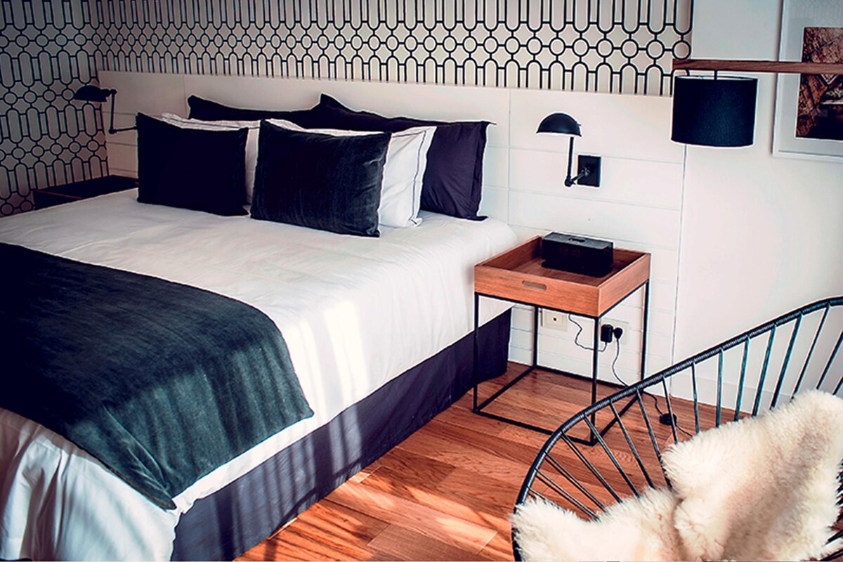 Una habitación de hotel moderna con una cama bien hecha, una mesita de noche con una lámpara y una silla.