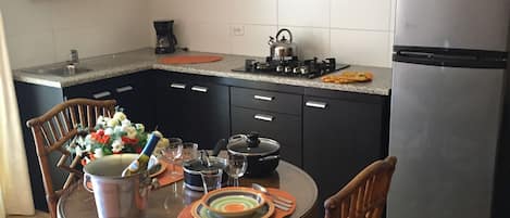 A compact kitchen with dark cabinets, a stainless steel refrigerator, and a dining table set with plates and a kettle.