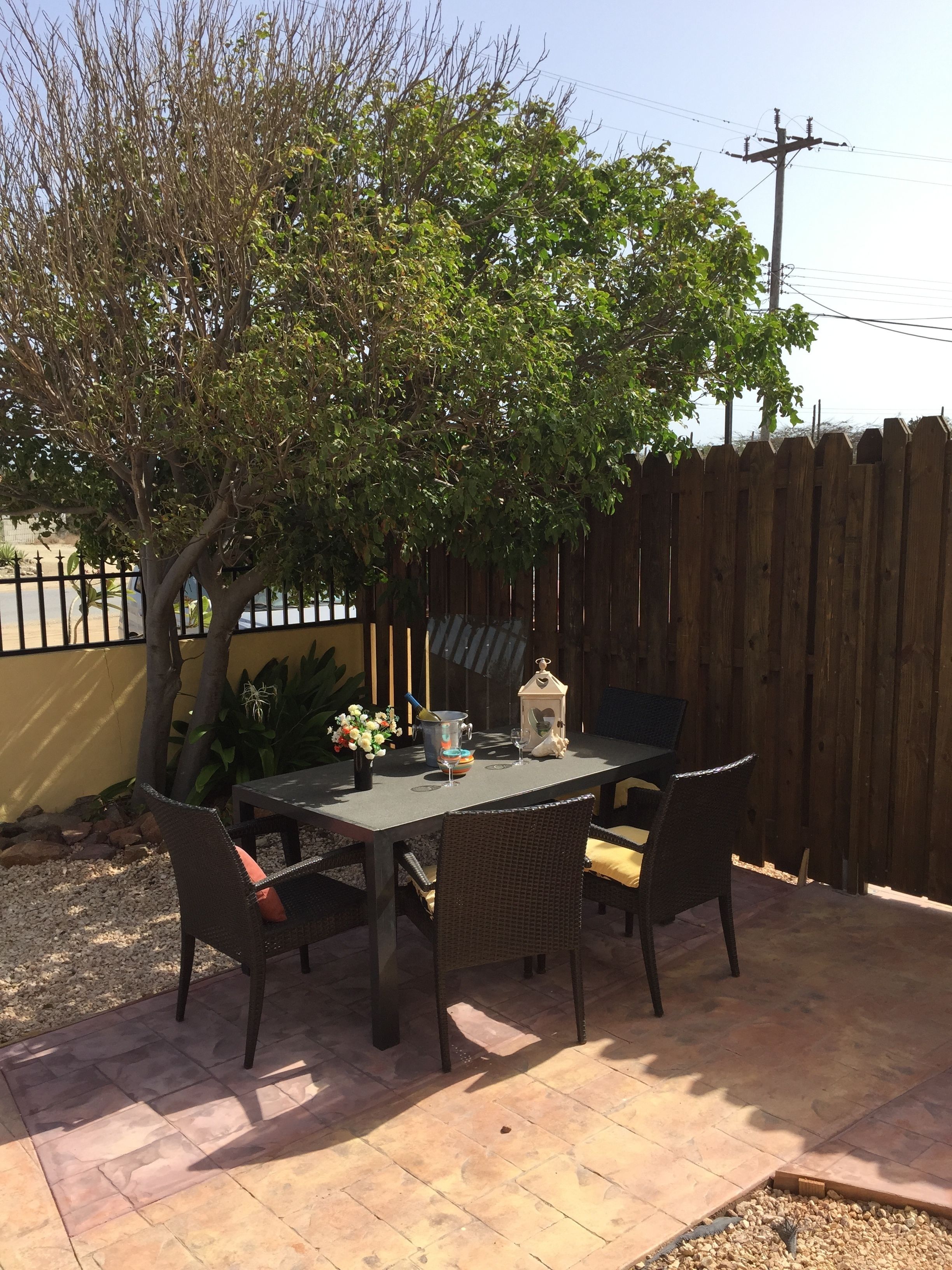 A patio with a table and chairs, surrounded by a wooden fence and a tree.