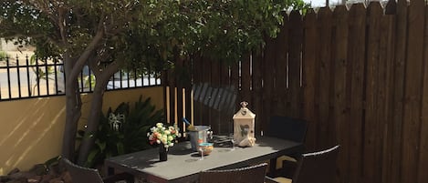 A patio with a table and chairs, surrounded by a wooden fence and a tree.