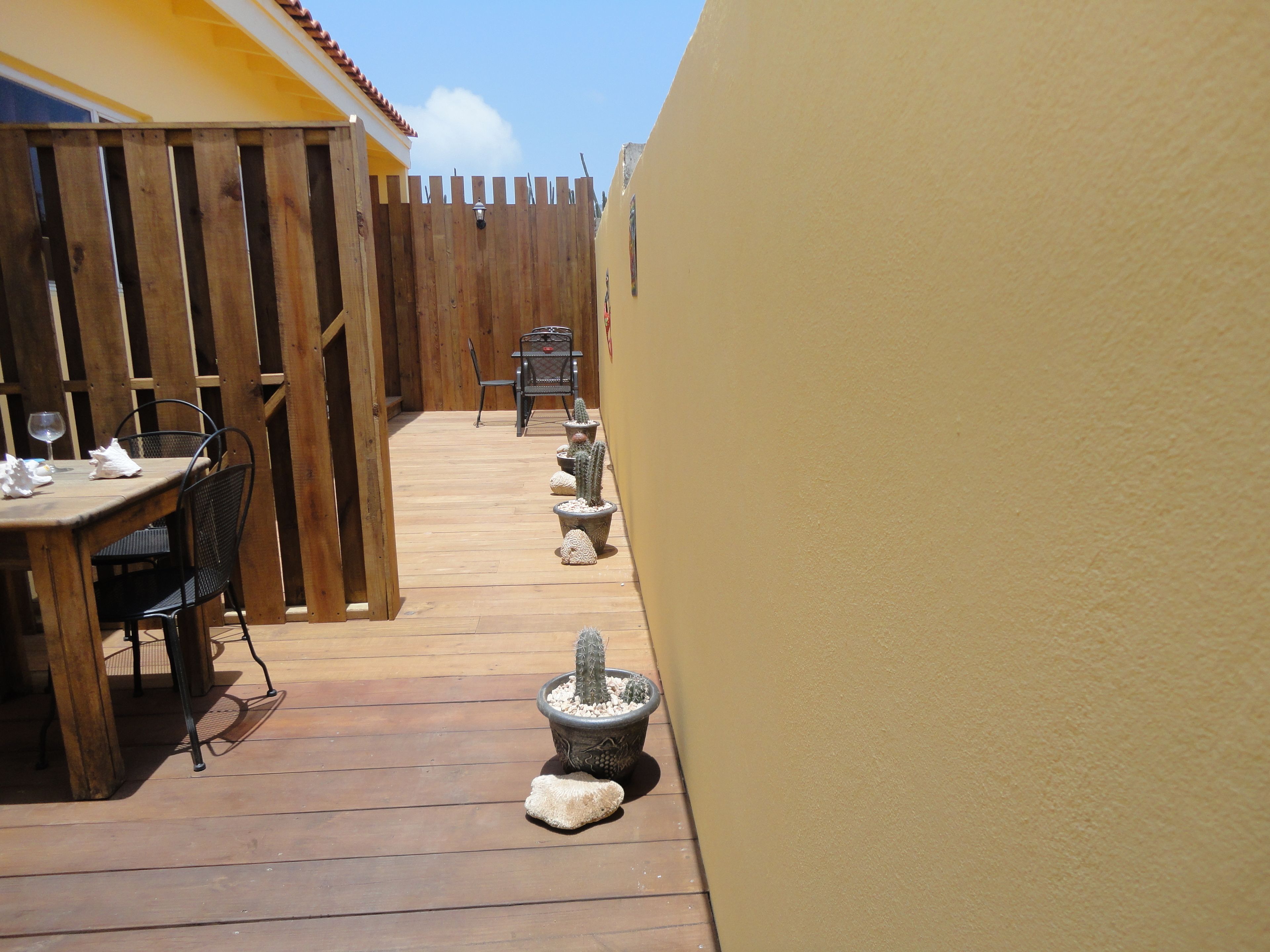 A wooden deck with a table and chairs, a wooden fence, and potted cacti.