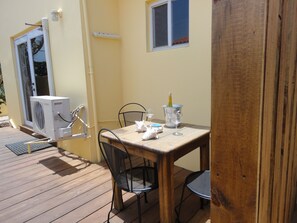An outdoor wooden deck with a table and chairs, a small window, and an air conditioning unit. - Alta Montaña Apartments (Noord)