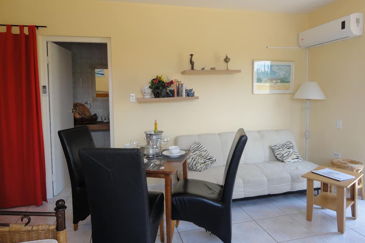 Un salon avec un canapé, une table à manger et des chaises, une petite table avec une lampe, et un rideau rouge.