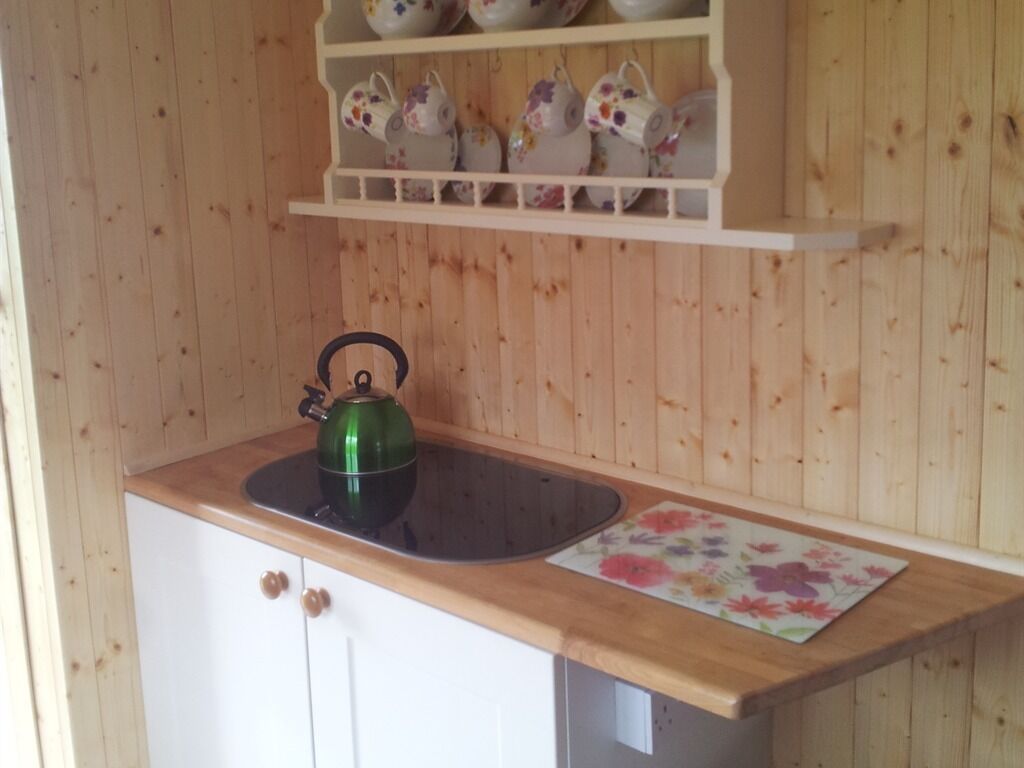 Ett kök med träskåp, en bänkskiva, en vattenkokare och en hylla med tekannor.