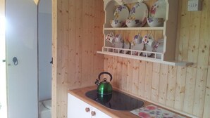 A kitchen with wooden walls, a white cabinet, a green kettle, and a shelf with floral-patterned dishes. - Shepherds Lodge (Worcester)