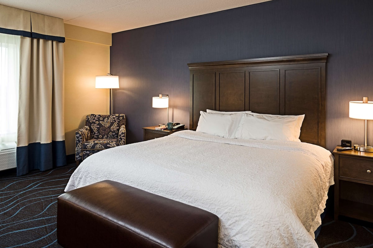 Habitación de hotel con una cama grande, una silla, dos mesitas de noche y una lámpara.