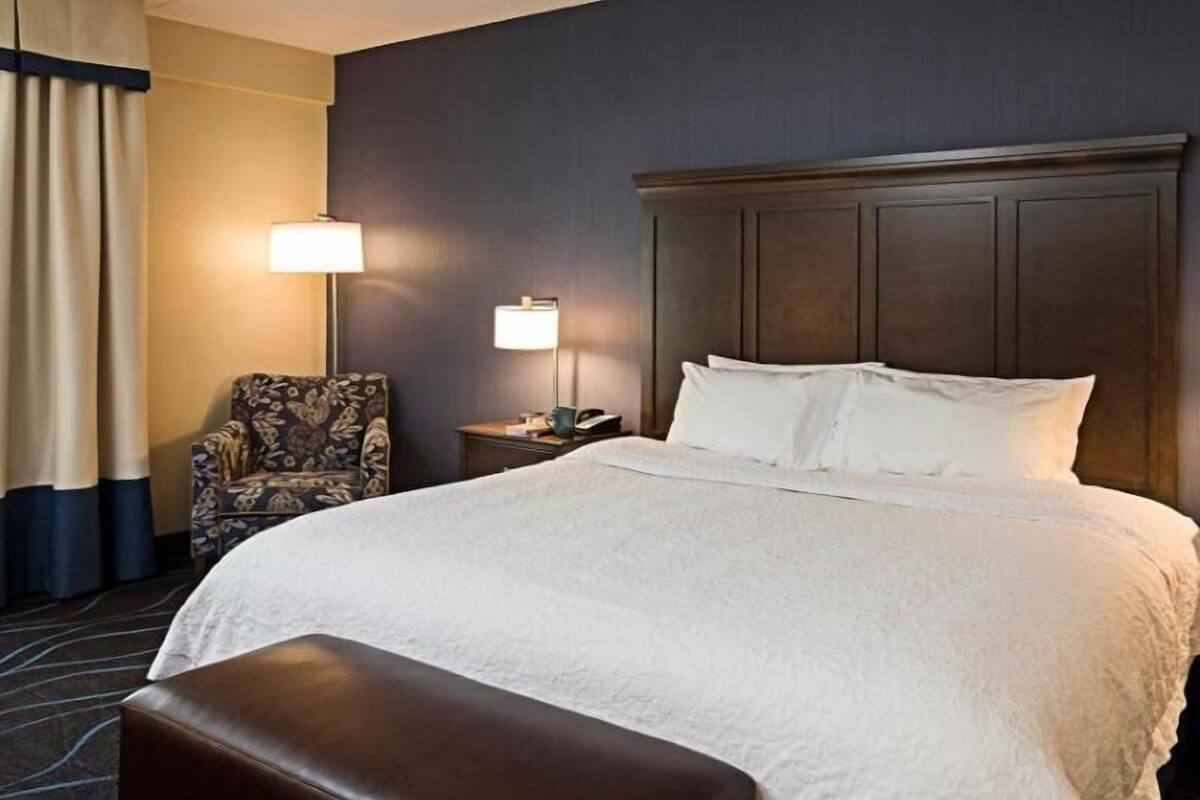 A hotel room with a large bed, a chair, a nightstand, and a lamp.