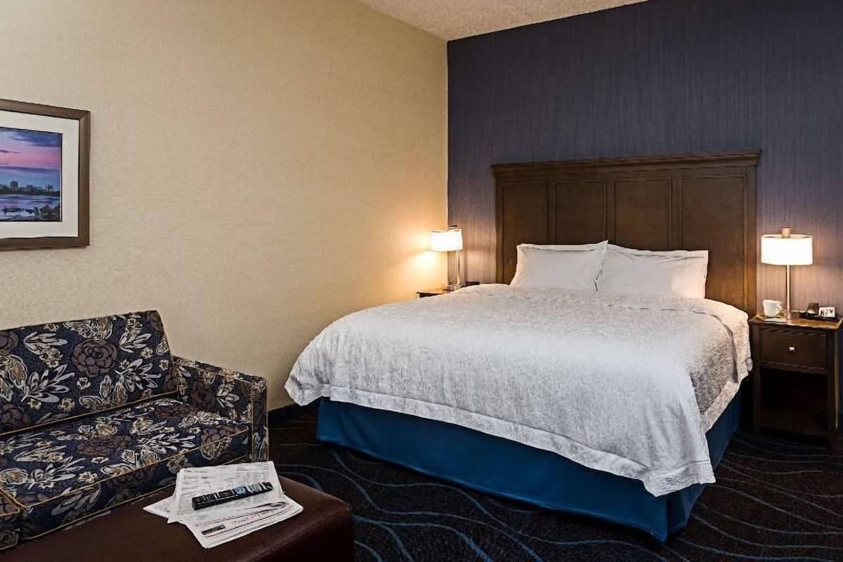 A hotel room with a bed, two bedside lamps, a sofa, and a framed picture on the wall.