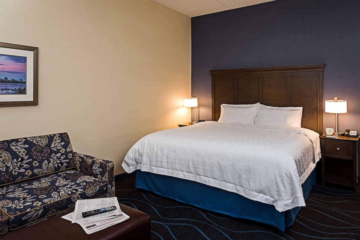 Una habitación de hotel con una cama, dos lámparas de noche, un sofá y un cuadro enmarcado en la pared.