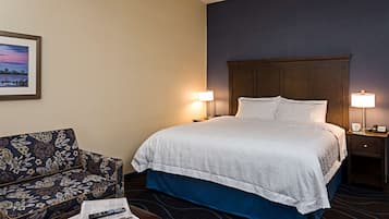 A hotel room with a bed, two bedside lamps, a sofa, and a framed picture on the wall.