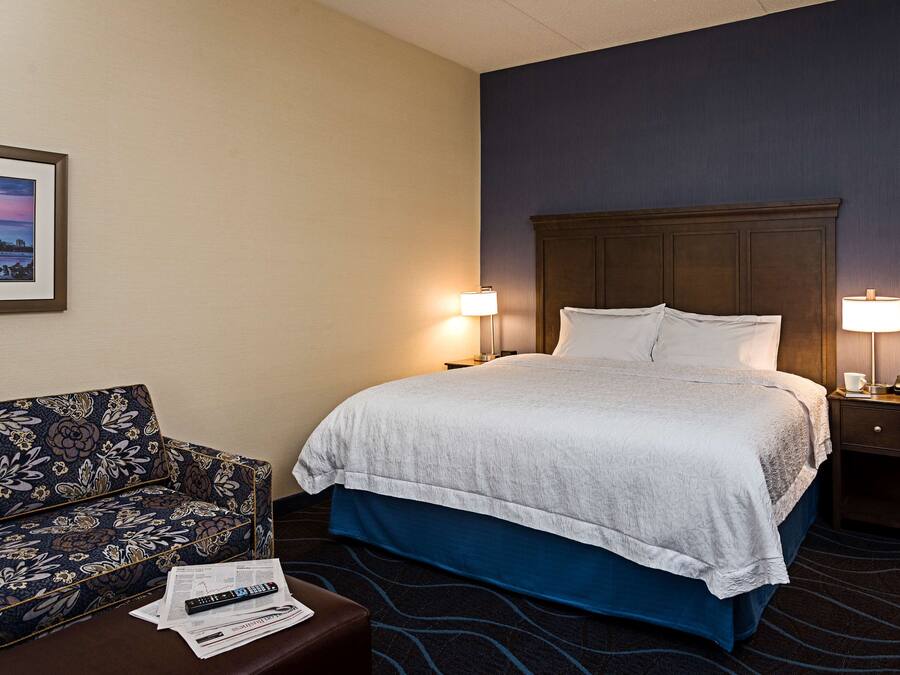 A hotel room with a bed, two bedside lamps, a sofa, and a framed picture on the wall.