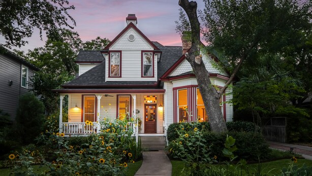 A two-story house with a front porch, a visible entryway, and a garden with sunflowers. - Brava House Bed and Breakfast (Austin)