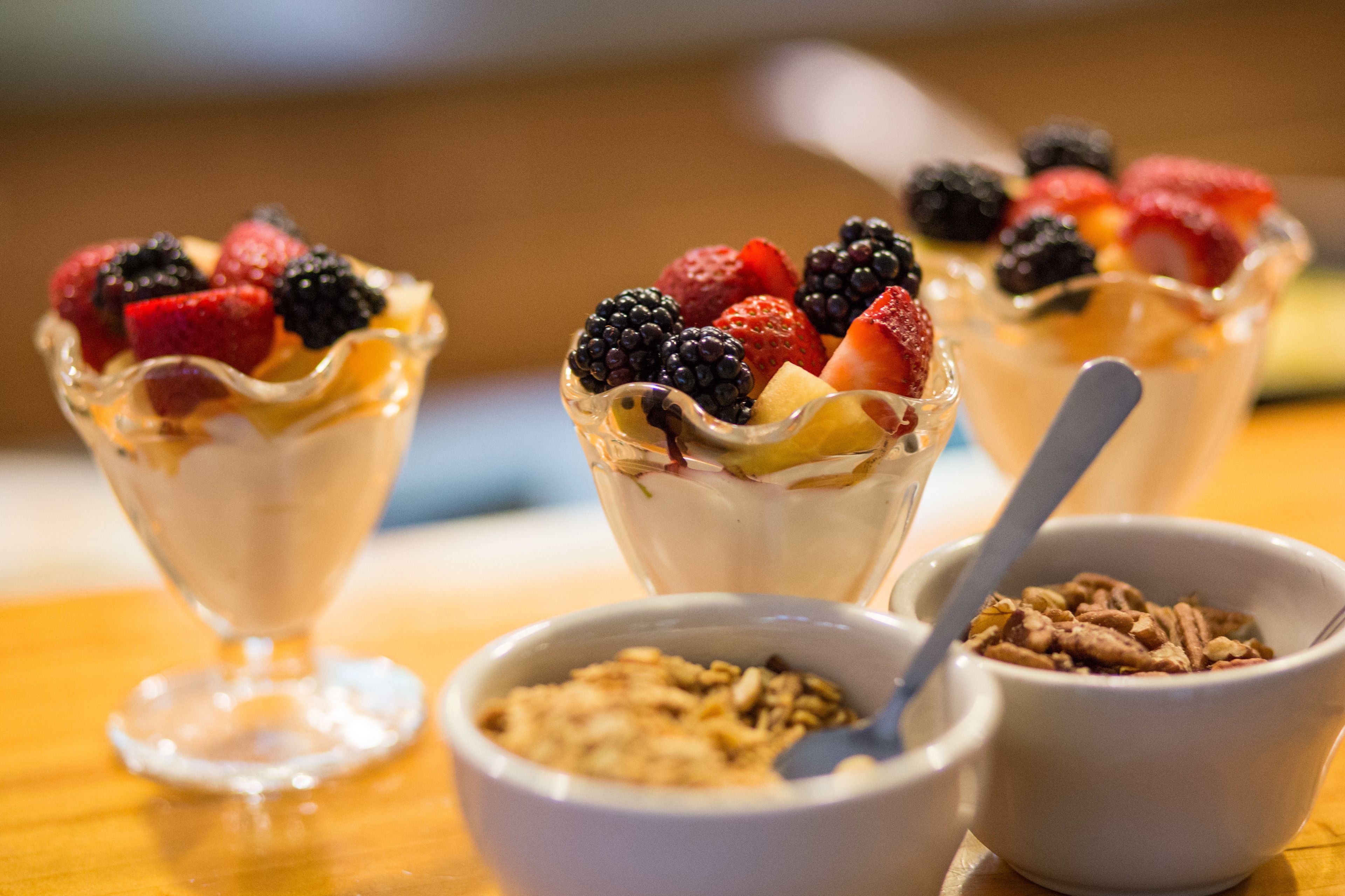 Three dessert glasses with fruit toppings, a bowl of granola, and a bowl of cereal.