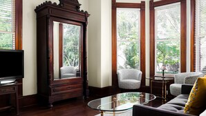 A living room with a large wooden cabinet, a glass coffee table, and patterned sofas. - Brava House Bed and Breakfast (Austin)