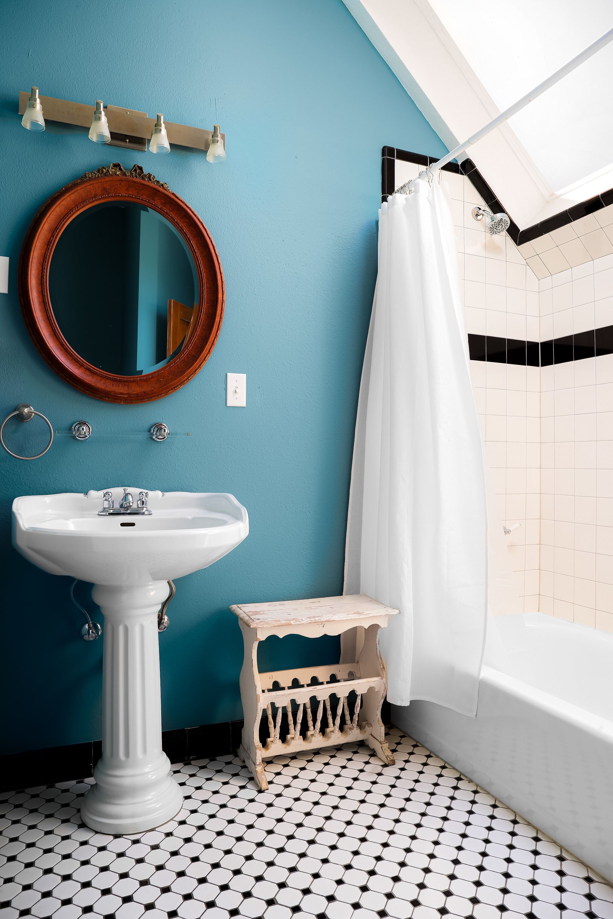 A bathroom with a white pedestal sink, a wooden vanity, a mirror, and a shower with a white curtain.