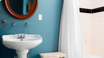 A bathroom with a white pedestal sink, a wooden vanity, a mirror, and a shower with a white curtain.