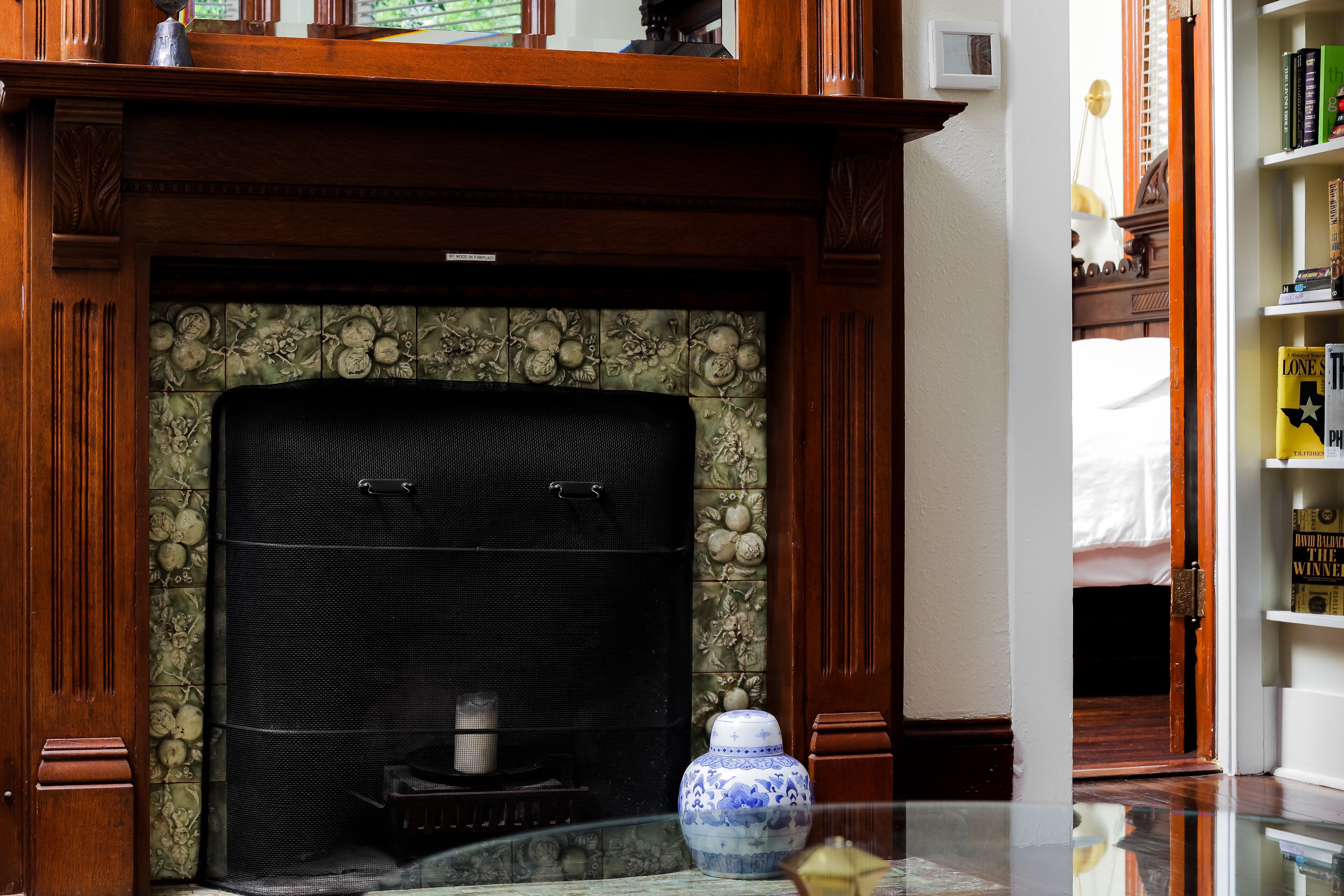 Une cheminée agrémentée d’un paravent décoratif, un vase posé sur le manteau de la cheminée et une bibliothèque sur le côté droit.