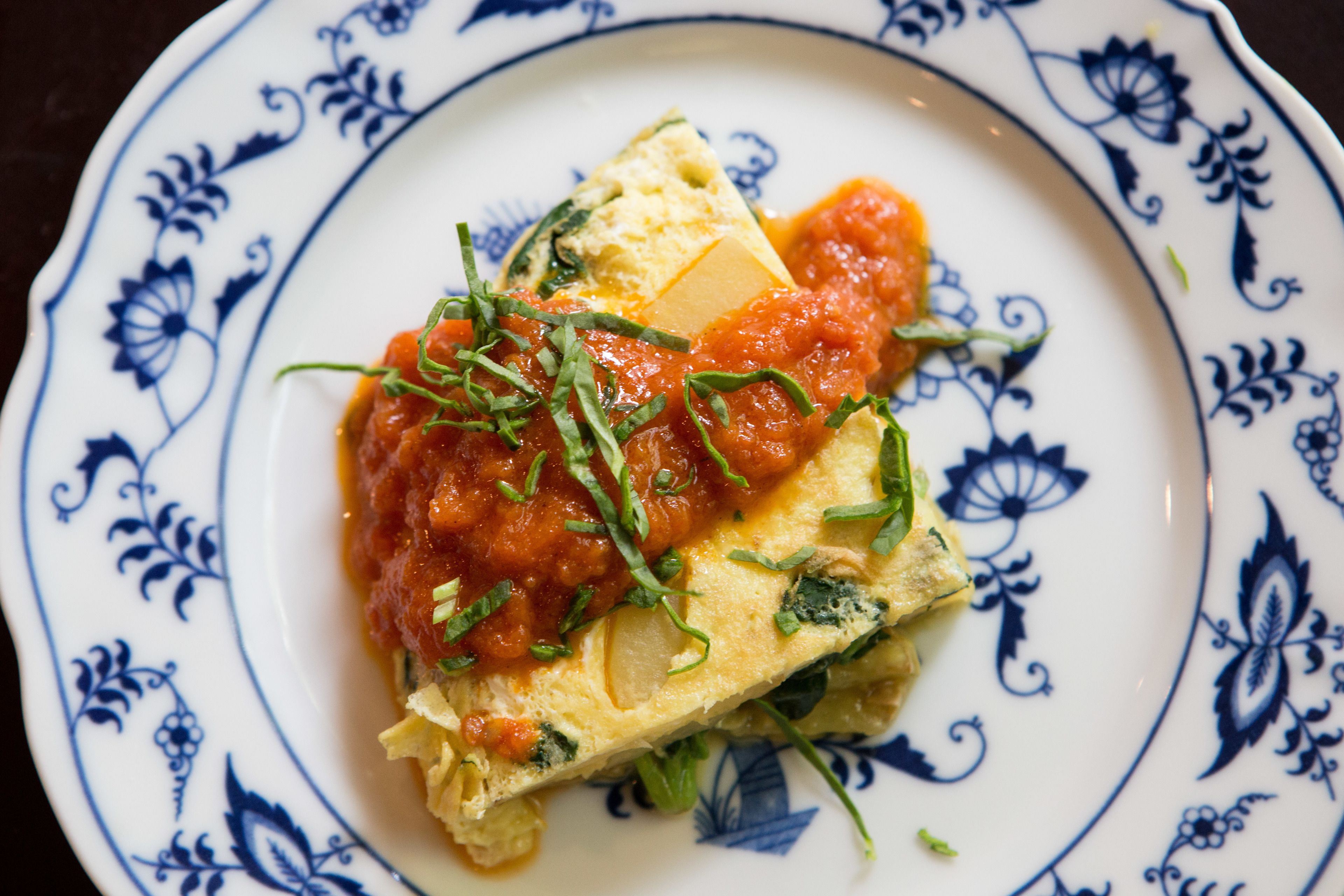 A plate with a slice of pizza topped with tomato sauce and cheese, garnished with herbs.