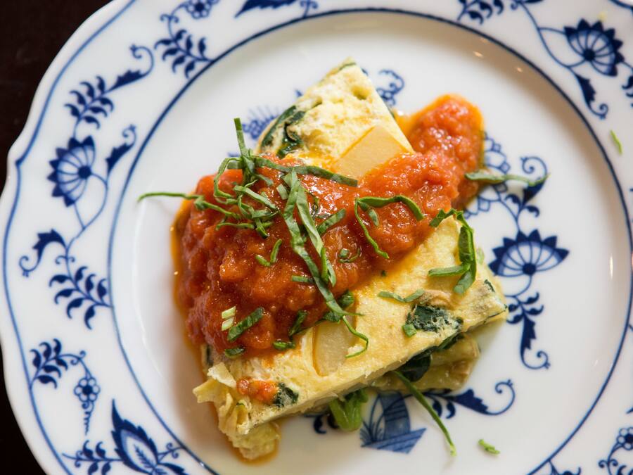 Une assiette contenant une part de pizza recouverte de sauce tomate et de fromage, et décorée d’herbes.