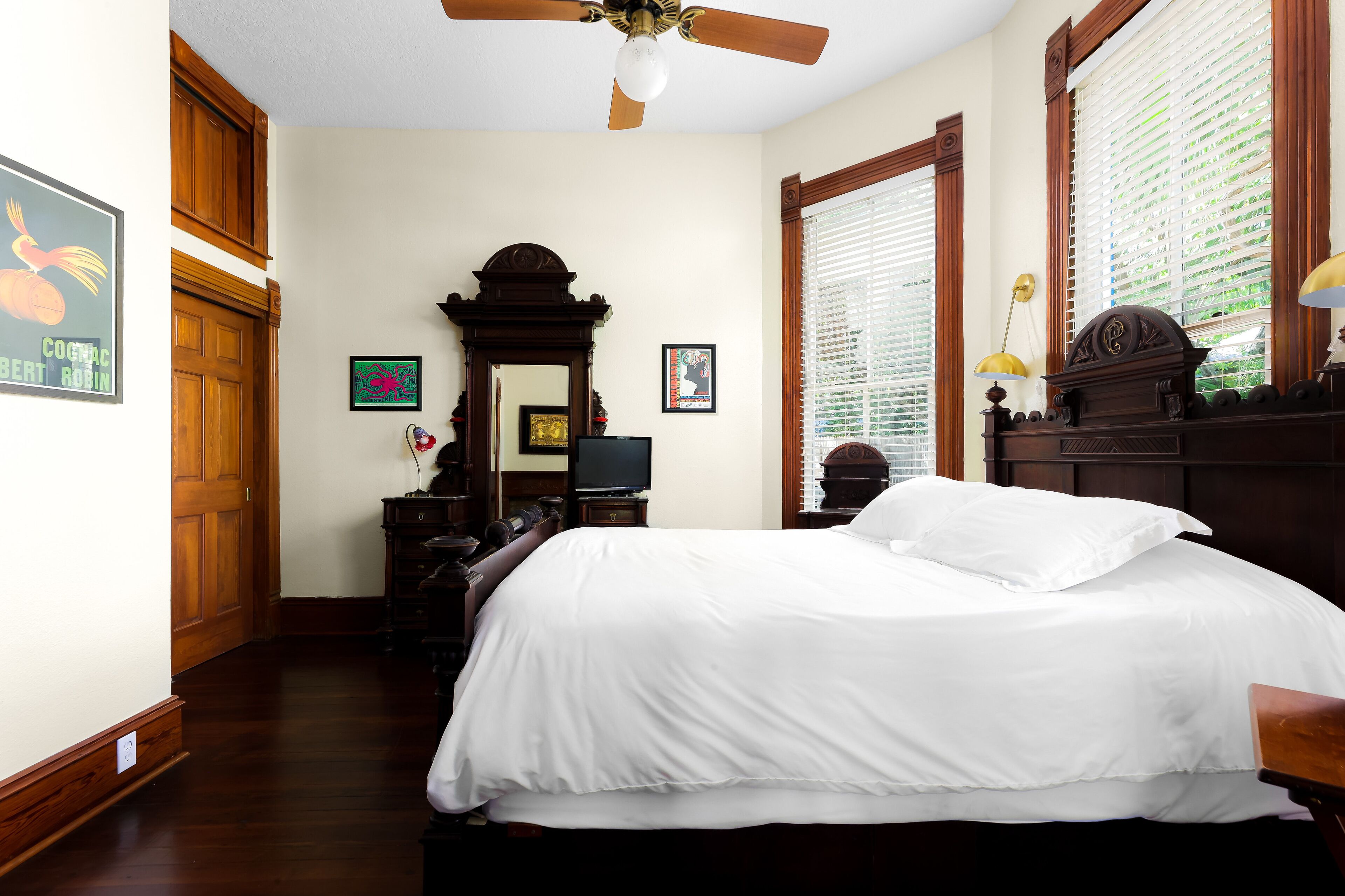 A hotel room with a large bed, wooden furniture, a ceiling fan, and a television.