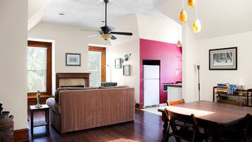A spacious living area with a large wooden dining table, a sofa, and a ceiling fan.