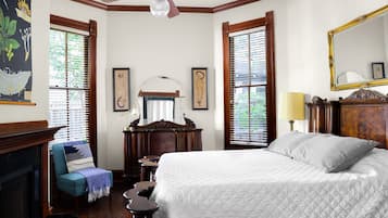 Een slaapkamer met een groot bed, een stoel met een plaid, een dressoir, een spiegel en een open haard.