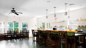 A spacious kitchen with a bar area, wooden chairs, and a ceiling fan. - Brava House Bed and Breakfast (Austin)