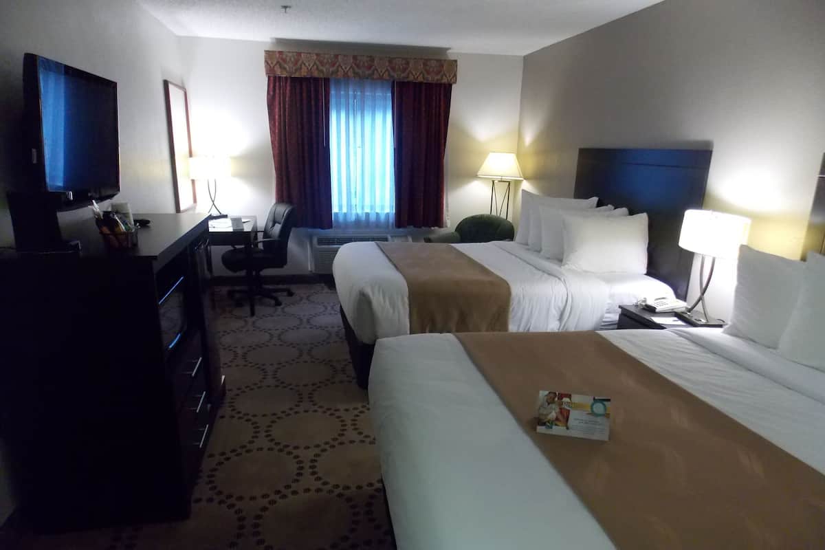 A hotel room with two beds, a desk, a television, and a window with curtains.