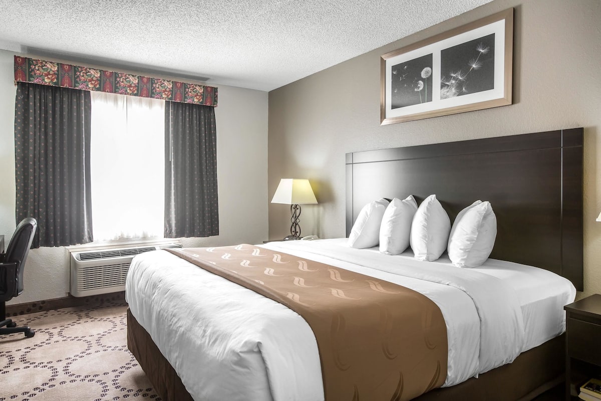 A hotel room with a bed, a desk, a chair, a lamp, and a framed picture on the wall.
