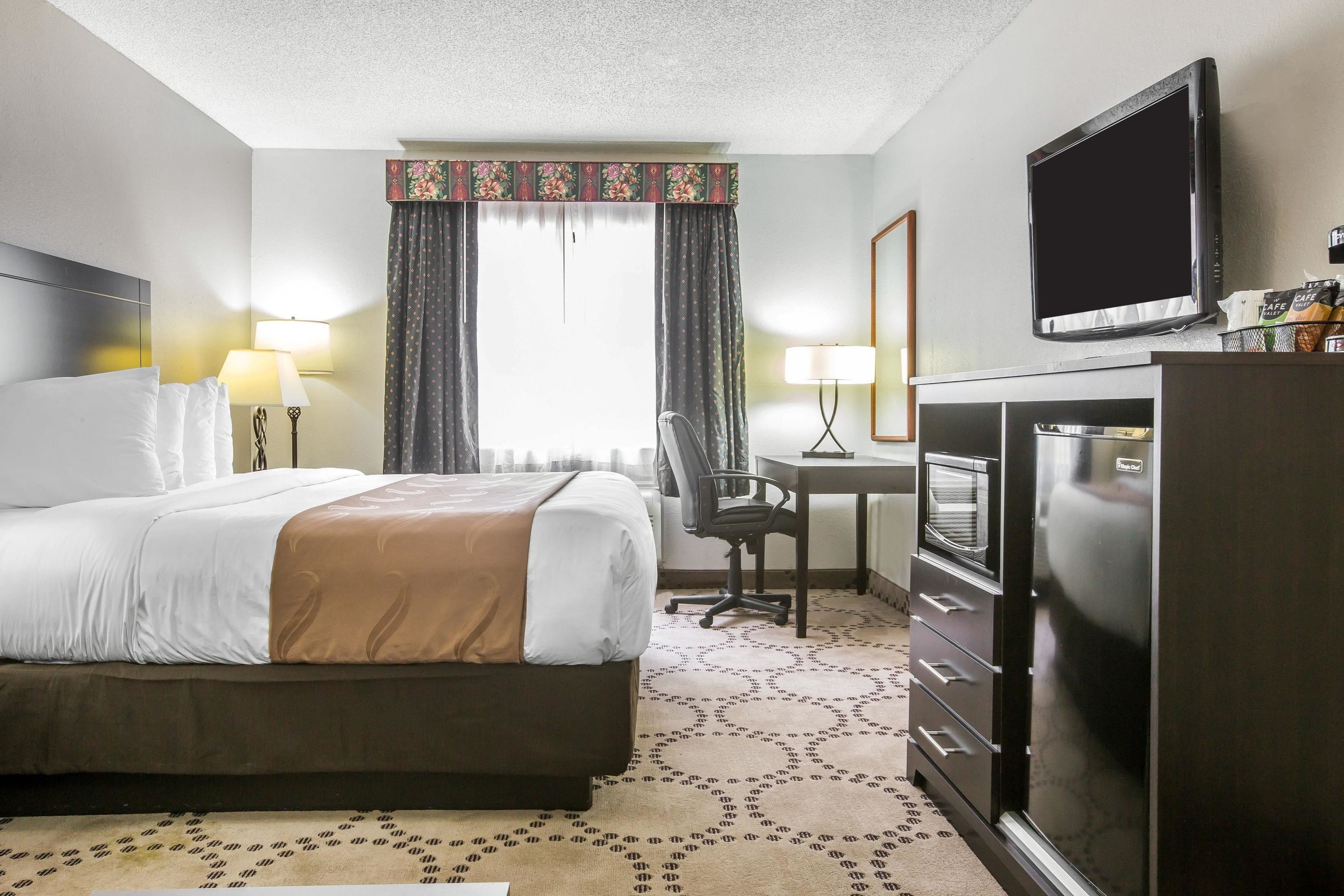 A hotel room with a bed, a desk, a chair, a television, and a minibar.
