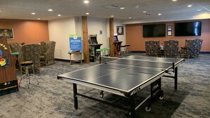 A ping pong table in a room with multiple chairs, a small table, and a TV screen on the wall. - Longhollow Point Inn Studio 1105 (Galena)