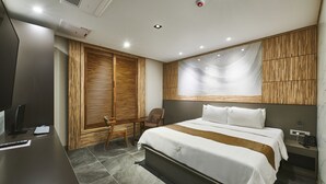 A modern hotel room with a large bed, a desk with a computer, a chair, and a wooden wardrobe. - Hotel Aura (Ansan)